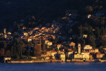 Torno.  View across Lake Como towards town spread across hillside in golden sunlight.