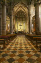 Interior of Church Sant Anastasia dating from the thirteenth century.  Painted vaulted ceiling  altar and crucifix  rows of pews on red  black and white patterned floor.