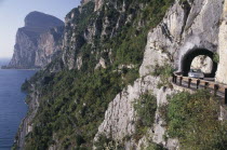 Car on high Gardesana Occidentale road with tunnels through cliff beside Lake Garda near Limone.