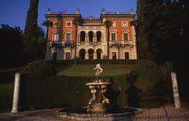 Private villa and formal gardens near Tremezzo  stone fountain in immediate foreground with lawn enclosed by hedge and grand facade of house behind.