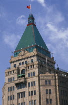 The Peace Hotel on the Bund.  Detail of exterior tower with green rooftop and Chinese flag flying from the top.