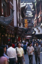 Yu Gardens  Old City.  Crowds of shoppers on narrow street lined by buildings with pagoda style tiled rooftops.