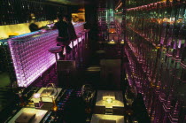 Tou Ming Si Kao   TMSK   bar interior with couple sitting at glass bar illuminated with coloured light.  Table laid with glasses and cutlery and lit by candles in foreground.