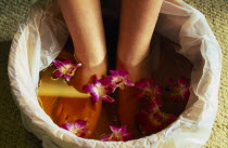 Bodhi Theraputic Retreat.  Close cropped shot of feet soaking in water scattered with orchid flowers.