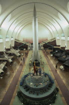 Interior hall of the Chinese Military Museum with visitors looking at display of military aircraft  tanks and missiles.