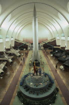 Interior hall of the Chinese Military Museum with visitors looking at display of military aircraft  tanks and missiles.