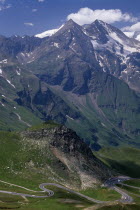View towards Glockner Group and the Grossglockner Road from Edelweisse-spitze view point.  Jagged points with snow lying in crevices of peaks  grassy lower slopes.