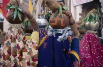 Back view of crowd of women carrying metal and earthenware pots on their heads with offerings of coconuts.