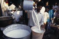 Street market scene with man pouring milk into bucket.