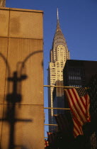 Part view of the Chrysler Building from East 42nd Street.  Seen above tower blocks and line of Stars and Stripes flags with shadow of street lamp on wall in foreground.Steel framed Art Deco skyscrap...