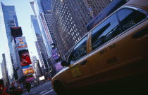 Times Square.  Yellow taxi cab on street with skyscraper buildings and illuminated advertising.
