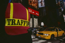 Times Square.  Traffic police officer wearing florescent jacket standing beside road with back to camera. Yellow taxi cab and other traffic waiting at pedestrian crossing.
