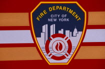 Detail of New York fire department badge on side of fire engine or truck.  Continues to depict city skyline including twin towers of the World Trade Centre.