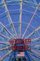 Coney Island.  Ferris wheel painted blue and orange with sign in red  Wonder Wheel  and American Stars and Stripes flag below.  Cropped to fill frame.