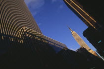 Part view of the Empire State Building from West 31st Street.  Angled view seen in sunlight at end of street framed by buildings in foreground partly in shadow. Designed by architect William Lamb of...