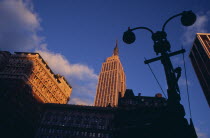 Part view of the Empire State Building from 7th Avenue / West 31st Street in orange sunlight with silhouetted street light and buildings in deep shadow in foreground. Designed by architect William L...