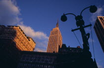 Part view of the Empire State Building from 7th Avenue / West 31st Street in orange sunlight with silhouetted street light and buildings in deep shadow in foreground. Designed by architect William L...