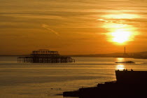 Remains of the West Pier silhouetted against a dramatic orrangy-red sunset  with a flock of starlings circling above it