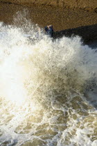 Waves crashing onto beach and groyne with people getting wet.