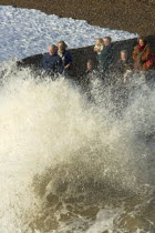 Waves crashing onto beach and groyne with people getting wet.
