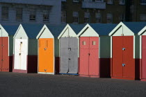 Multi-coloured beach huts on the tarmac promenade with block of flats in the background.