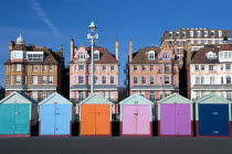 Multi-coloured beach huts on the tarmac promenade with old houses in the background.
