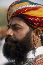 Head and shoulders side profile portrait of a Mr Desert contestant with a beard wearing a colourful turban and traditional earrings at the Desert Festival