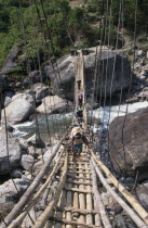 Crossing a sagging suspension bridge over the Khudi Khola at Khudi. Bridge made from woode with metal support wires.