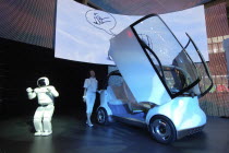 2007 Tokyo Car Show  Honda exhibit  Asimo Robot presents Honda concept car Puyo  young woman opens cars gull-wing doors