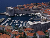 Elevated view over the Old City Harbour with fortified walls. Yachts moored in marina surrounded by buildings with terracotta tiled rooftops