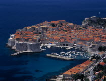 Elevated view over the Old City Harbour with fortified walls. Yachts moored in marina surrounded by buildings with terracotta tiled rooftops