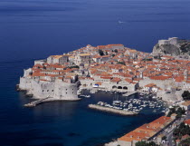 Elevated view over the Old City Harbour with fortified walls. Yachts moored in marina surrounded by buildings with terracotta tiled rooftops