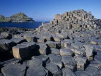 Interlocking basalt stone columns left by volcanic eruptions. View across the stones towards cliffs and coastline