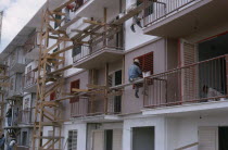 Construction workers and painters on wooden scaffolding working on muli-storey building exterior.