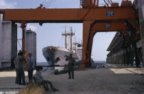 Soldiers in dockyard with container ship moored behind framed by huge steel crane.