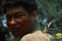 Portrait of young Campa tribesman with red and black painted face looking towards camera over his shoulder.