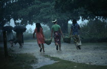 Tongan women carrying woven baskets between them through monsoon rain.