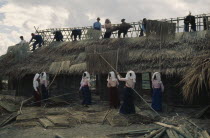 Tia minority men and women working together to thatch building.