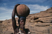 Dogon woman carrying clay pot of beer on her head to nearby village.