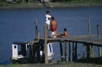 Amazon Estuary.  Man having a haircut while waiting for the ferry on wooden jetty watched by two children.