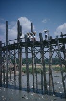Women carrying baskets on their heads crossing high wooden bridge across river and ducks.