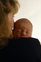 Mother holding face against three week old son carried on her shoulder.