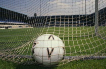 Close shot of football in back of net of goal on soccer pitch.
