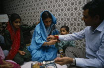 Woman tying thread on wrist of man during the Sacred Thread ceremony. The Hindu male rite of passage ceremony