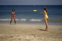 Two women wearing bathing costumes playing Frisbee on sandy beach next to the sea in St Ives  Cornwall  England
