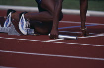 Detail of lower half of a runner holding a batton in a relay race with feet in the starting blocks
