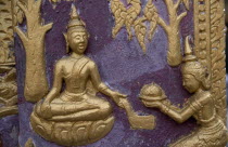 Wat Xieng Thong.  Temple detail of gold painted relief carving on purple background depicting seated Buddha receiving offerings.