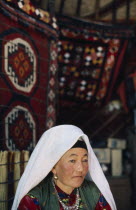 Kirghiz woman sat in yurt wearing traditional dress.