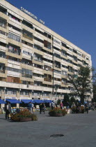 Street scence with people selling paintings in front of shops and apartrments.