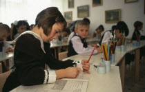 Young female student writing in classroom of boys and girls.